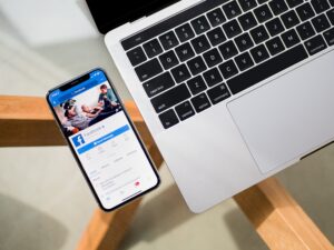 facebook on screen of phone next to laptop on desk