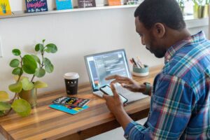 man at desk on his phone with a laptop open and a coffee