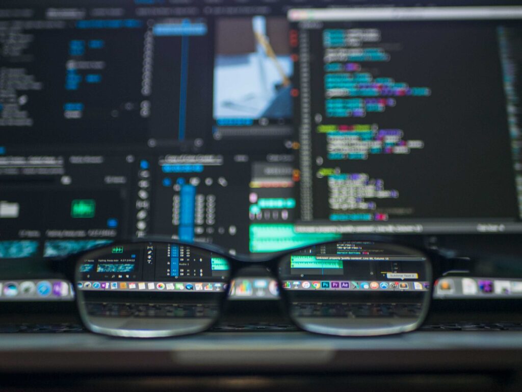 code on screen of two desktops with glasses in the forefront